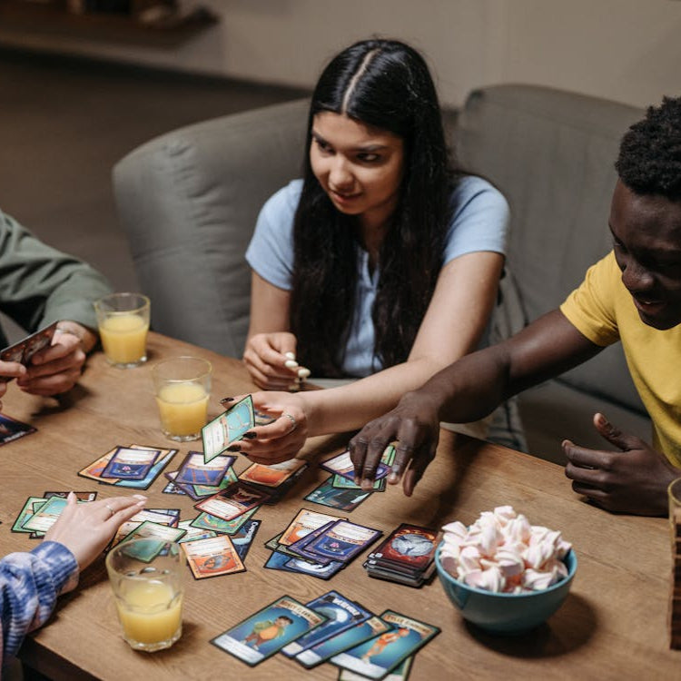 Four people playing a card game around a table with drinks and snacks.